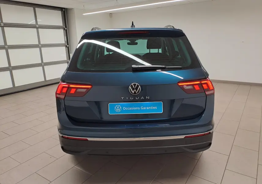 Vue arrière d'un Volkswagen Tiguan 2023 bleu Nightshade avec feux allumés et crochet d'attelage escamotable visible.