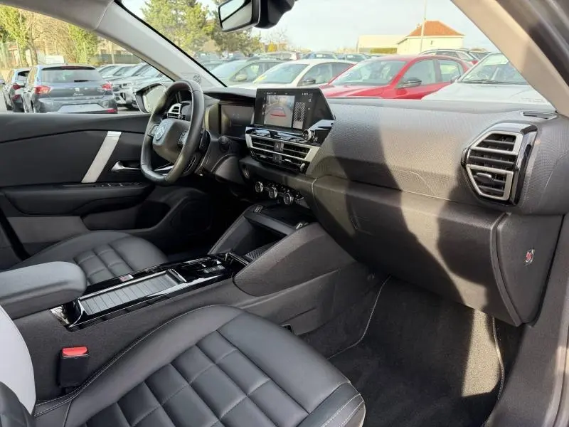 Vue intérieure côté conducteur du Citroën C4 X 2025 gris Mercury, avec tableau de bord moderne et sièges cuir noirs.