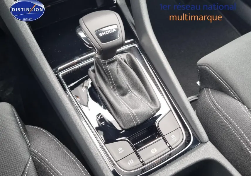 Gros plan sur la console centrale noire du Skoda Karoq 2025, avec levier de vitesse automatique et coutures blanches visibles.