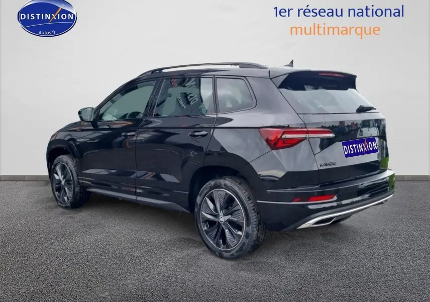 Vue 3/4 arrière droite d’un Skoda Karoq noir 2025 avec jantes alu noires et barres de toit visibles.
