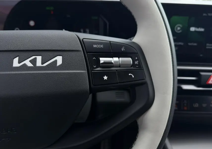 Gros plan sur le volant bi-ton clair du Kia Sportage 2026 avec commandes multifonctions à droite et logo Kia visible.