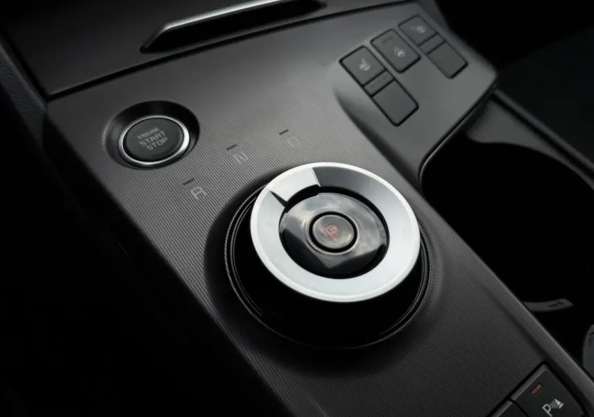 Gros plan sur la molette de sélection de vitesse et bouton start/stop dans l’habitacle noir du Kia Sportage gris lunaire.