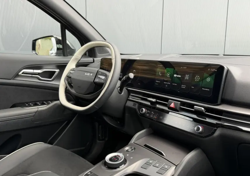 Vue intérieure côté conducteur du Kia Sportage 2026, volant bi-ton et écran tactile large sur tableau de bord noir.