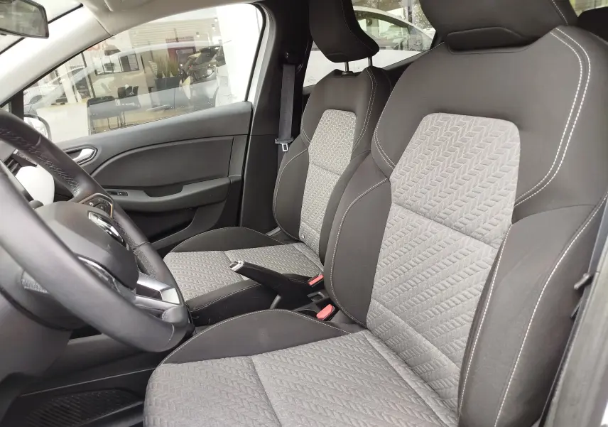 Vue intérieure côté conducteur de la Renault Clio 2023, sièges tissu gris à motifs géométriques et volant cuir noir.