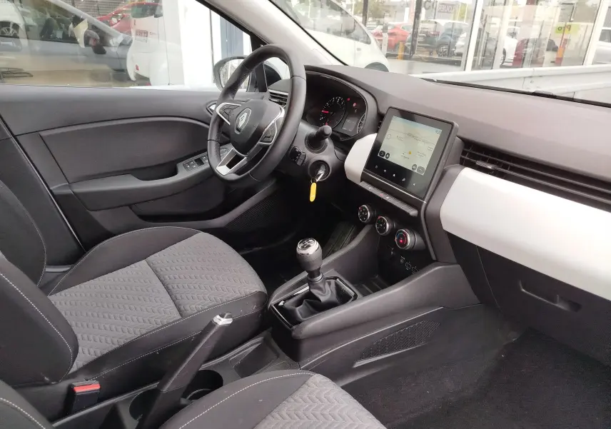 Intérieur de Renault Clio 2023 vu côté conducteur, tableau de bord gris clair avec écran tactile et boîte manuelle.
