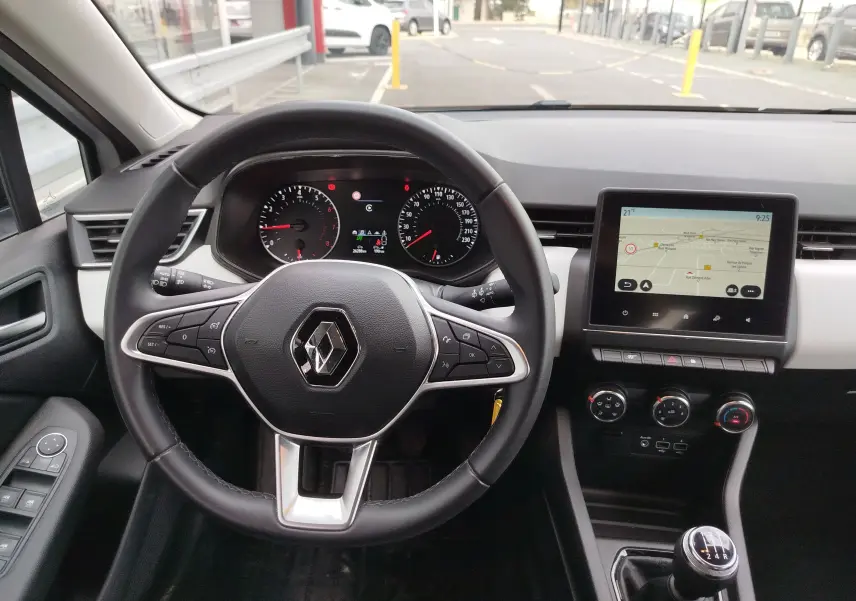 Vue intérieure frontale du poste de conduite de la Renault Clio blanche avec volant multifonction et écran tactile GPS.