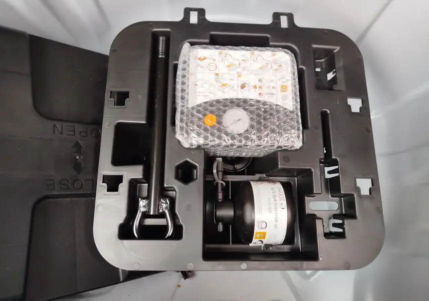 Kit de réparation de pneu Renault Clio 2023 en vue plongeante, avec compresseur et outil de levage rangés dans un compartiment noir.