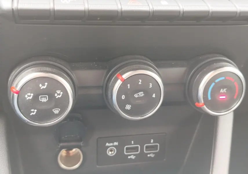 Gros plan sur les commandes de climatisation de la Renault Clio blanche, avec réglages manuels et port USB visibles.