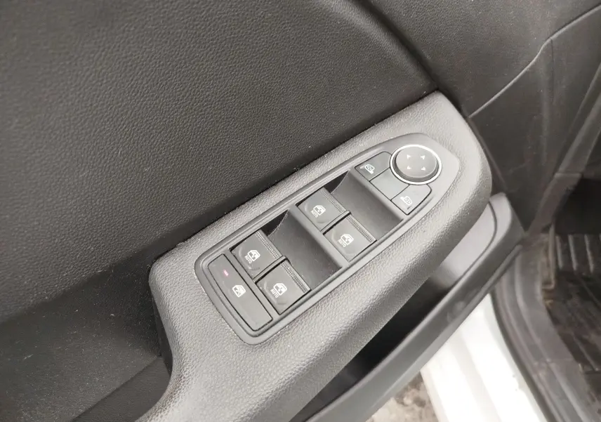 Gros plan sur la commande des vitres électriques côté conducteur d'une Renault Clio blanche, avec boutons noirs et réglage des rétroviseurs.