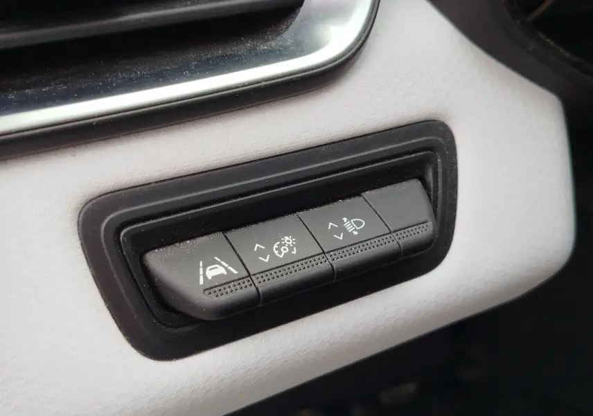 Gros plan sur les commandes noires du tableau de bord blanc glacé de la Renault Clio 2023, avec réglages d'assistance et éclairage.