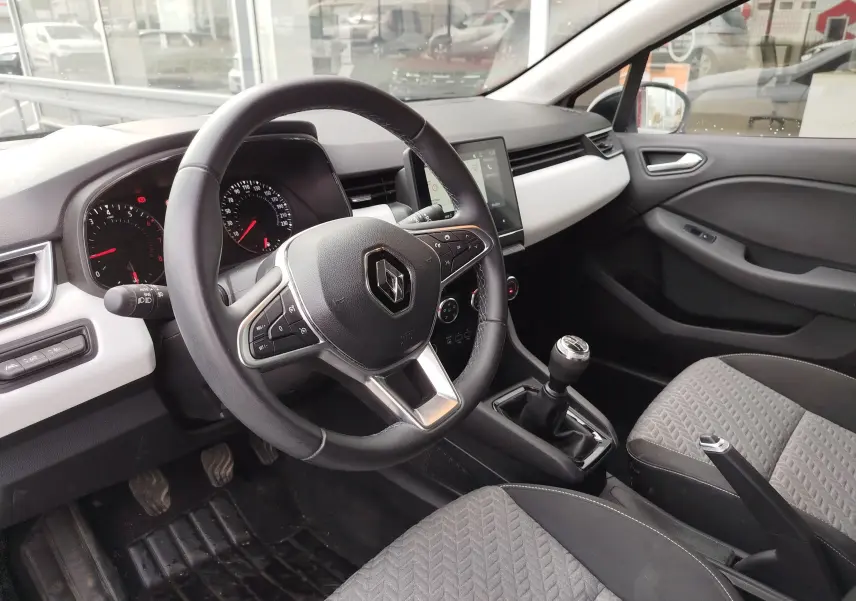 Intérieur de Renault Clio 2023 vu côté conducteur, volant multifonction, tableau de bord noir et blanc, levier de vitesse manuel.