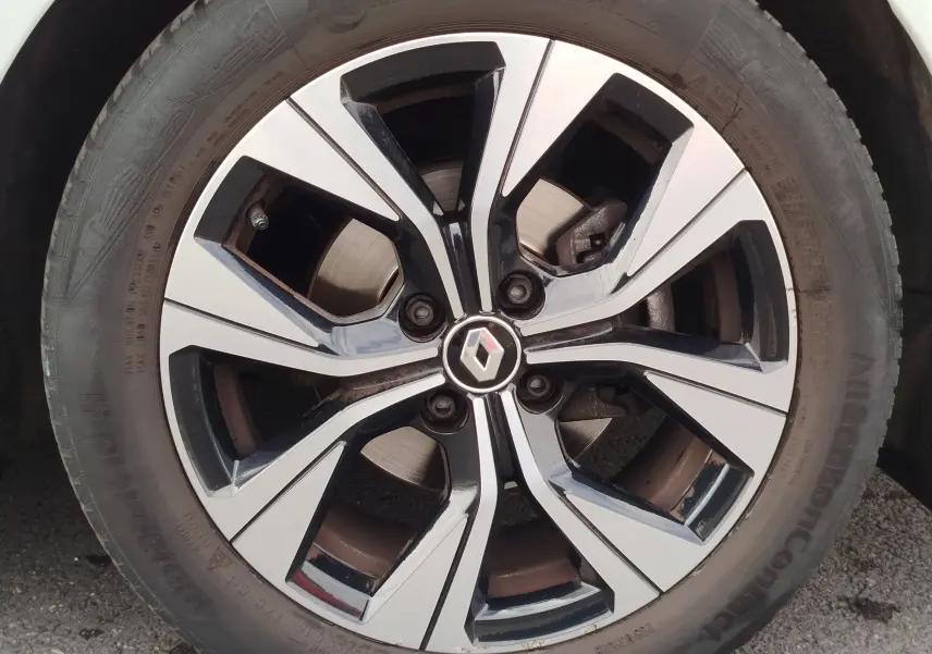Gros plan sur la jante alliage bicolore noir et argent avec logo Renault au centre d'une Renault Clio Blanc Glacier.
