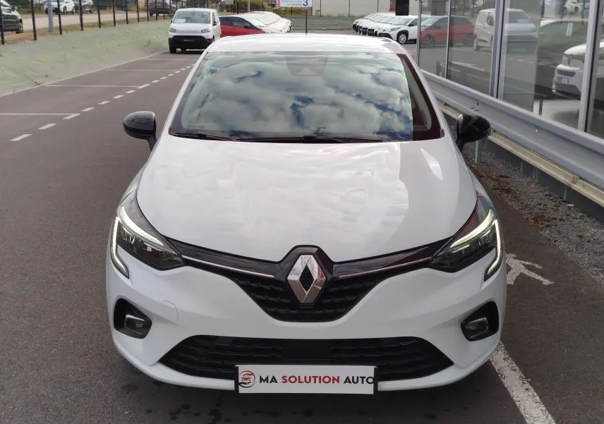Vue avant d'une Renault Clio 2023 blanc glacier avec phares LED allumés et calandre noire brillante.