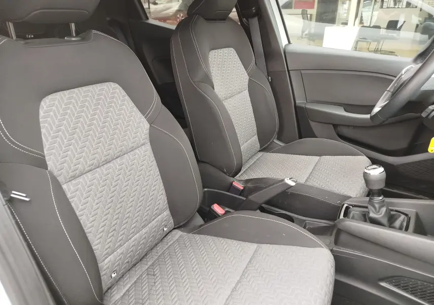 Vue intérieure côté conducteur de la Renault Clio 2023, sièges tissu gris avec surpiqûres blanches et levier de vitesse manuel.