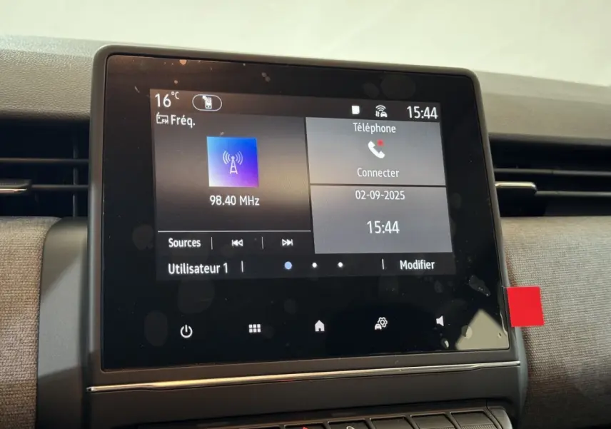 Écran tactile central de la Renault Clio gris clair affichant la radio et la connexion téléphone, vue rapprochée intérieure.