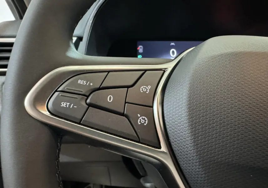 Gros plan sur les commandes du régulateur de vitesse au volant en cuir synthétique d'une Renault Clio gris clair 2025.