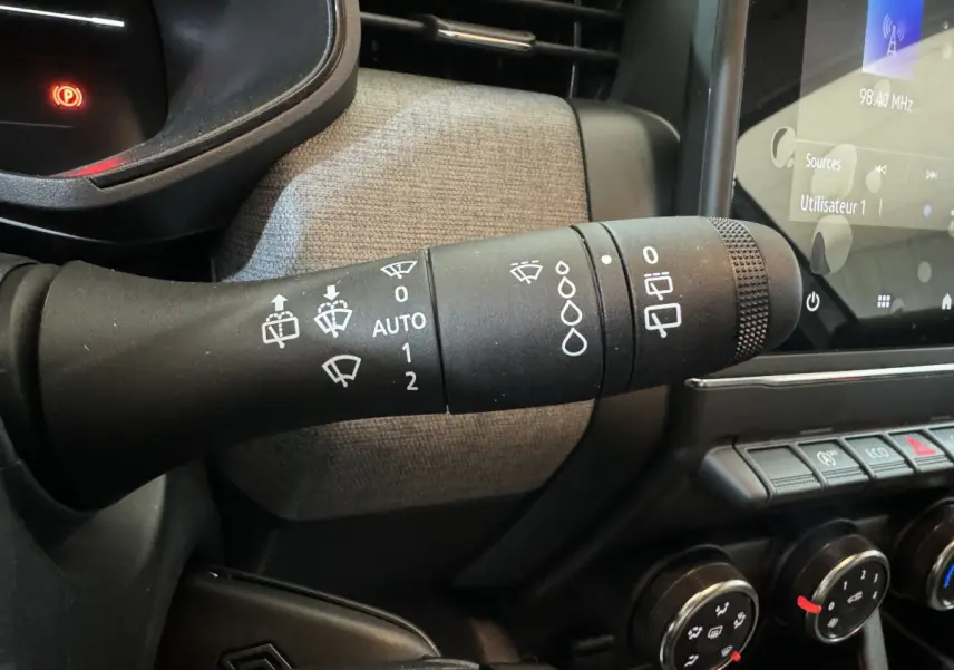 Gros plan sur la commande d’essuie-glace de la Renault Clio gris clair 2025, avec tableau de bord et écran tactile visibles.