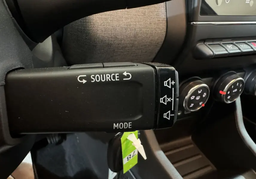 Gros plan sur la commande au volant de la Renault Clio gris clair 2025, avec boutons source et mode visibles.