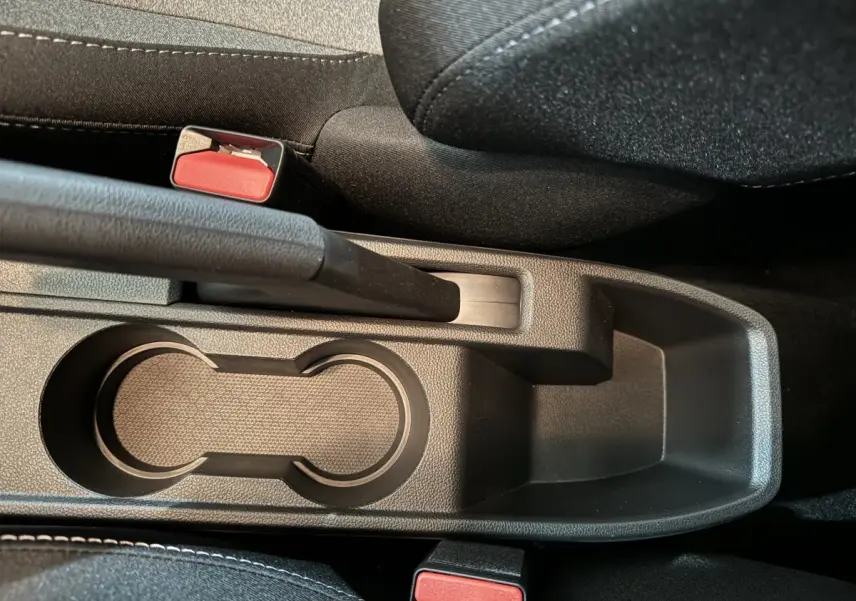 Gros plan sur la console centrale noire de la Renault Clio Evolution Blue dCi 100, avec frein à main et deux boutons de ceinture rouges.