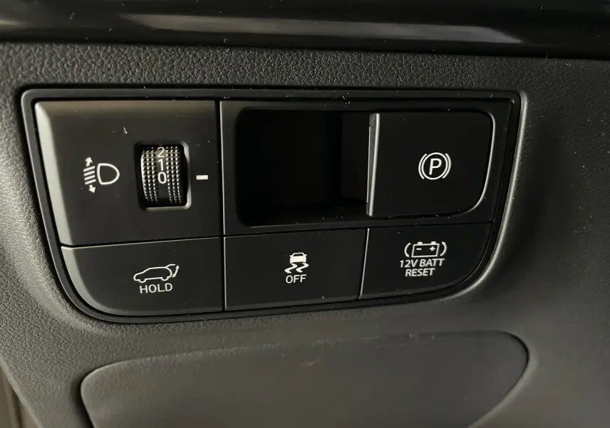 Gros plan sur les commandes noires du tableau de bord du Hyundai Tucson 2025, avec boutons de frein à main et réglage phares.