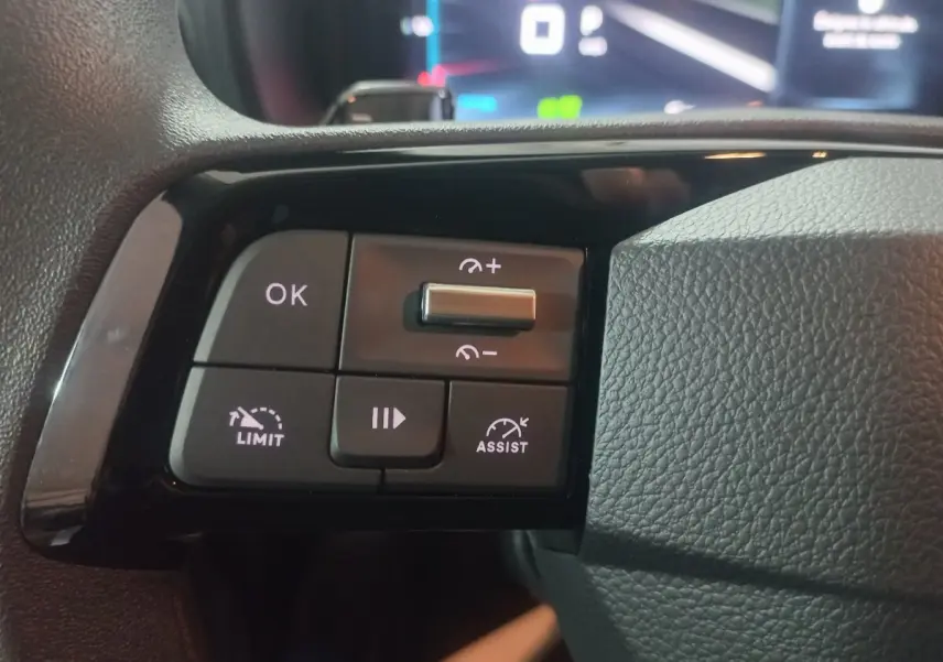 Gros plan sur les commandes multifonctions noires du volant du Citroën Berlingo XL blanc, avec affichage numérique flou en arrière-plan.