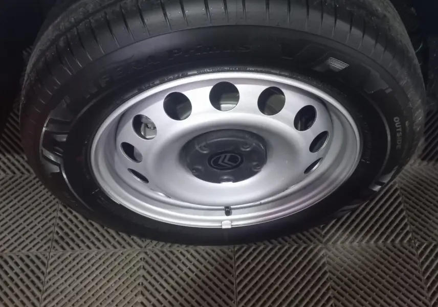 Gros plan sur la roue acier argentée avec logo Citroën, montée sur un pneu noir, sol en caoutchouc texturé visible.