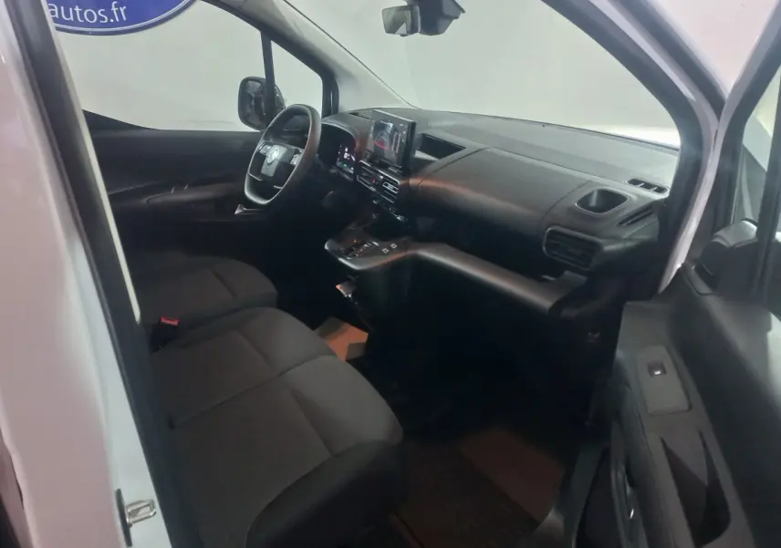 Vue intérieure côté conducteur du Citroën Berlingo blanc 2025, montrant le tableau de bord et les sièges avant noirs.