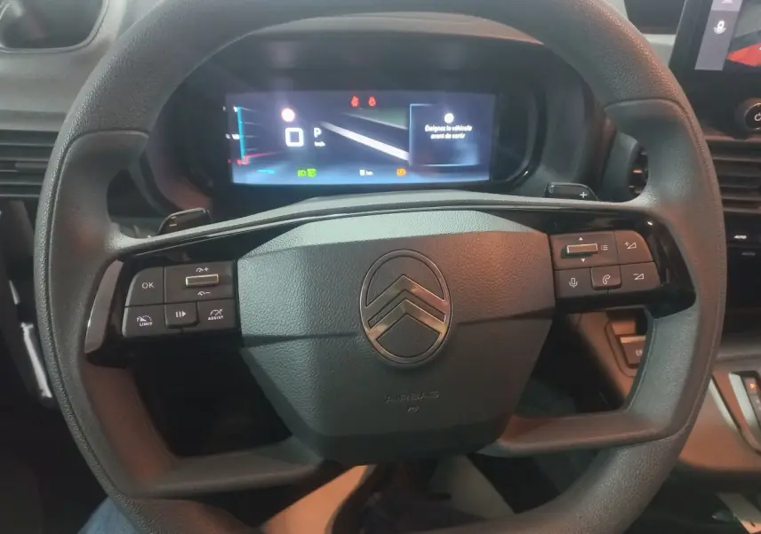 Vue rapprochée du volant multifonctions noir du Citroën Berlingo 2025 avec tableau de bord numérique allumé.