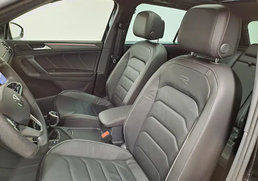 Vue intérieure côté conducteur du Volkswagen Tiguan 1.4 eHybrid 2023 avec sièges cuir noirs embossés "R" et finitions rouges.