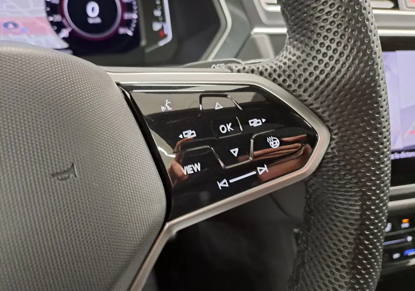 Gros plan sur les commandes multifonctions côté gauche du volant perforé noir du Volkswagen Tiguan 2023 hybride rechargeable.