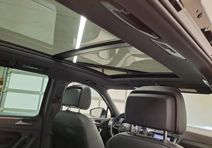 Vue intérieure avant du Volkswagen Tiguan 1.4 eHybrid 2023, toit panoramique et sièges en cuir noir visibles.