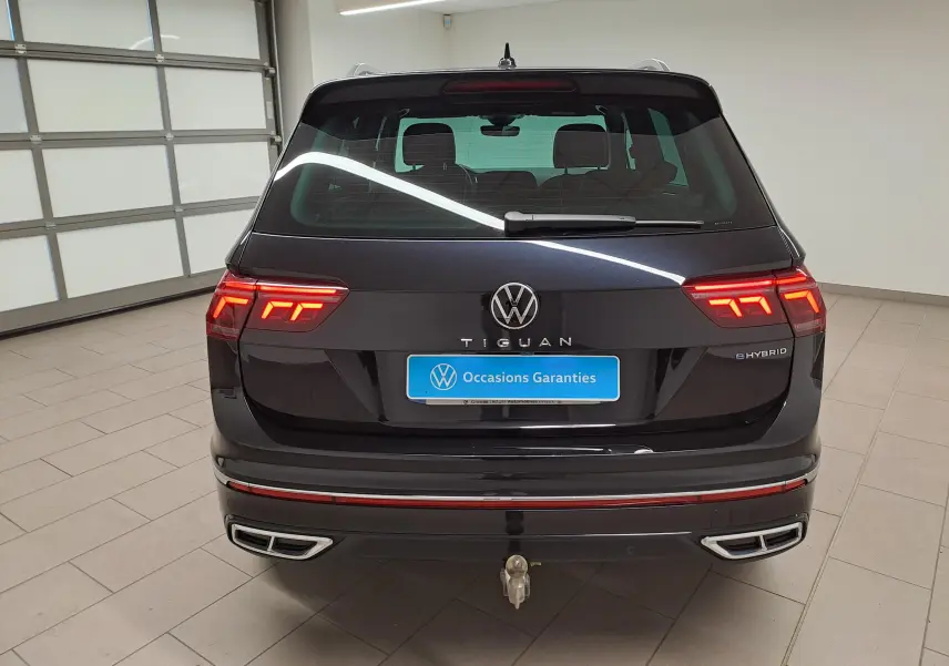 Vue arrière du Volkswagen Tiguan 1.4 eHybrid noir intense nacré avec feux allumés et crochet d'attelage escamotable visible.