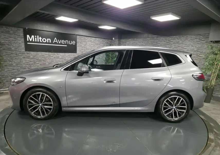 BMW Série 2 218i Active Tourer gris métallisé vue de profil côté gauche avec jantes alliage 18 pouces et vitres teintées.