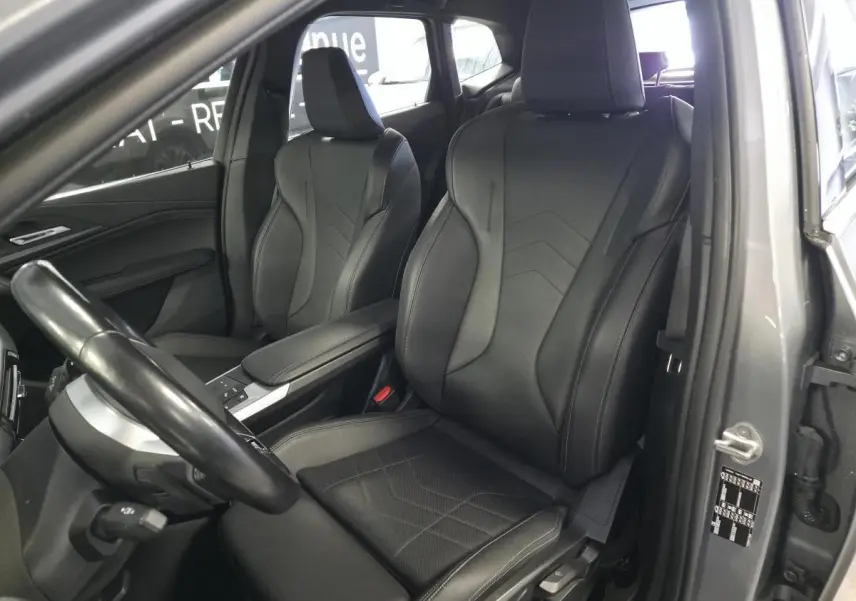 Vue intérieure côté conducteur de la BMW Série 2 218i Active Tourer 2023, sièges sport en similicuir noir et console centrale grise.