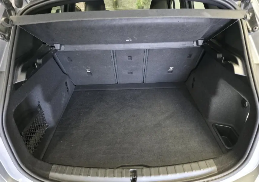 Coffre ouvert vu de l'arrière d'une BMW Série 2 218i Active Tourer gris avec tapis noir et filet de rangement latéral.