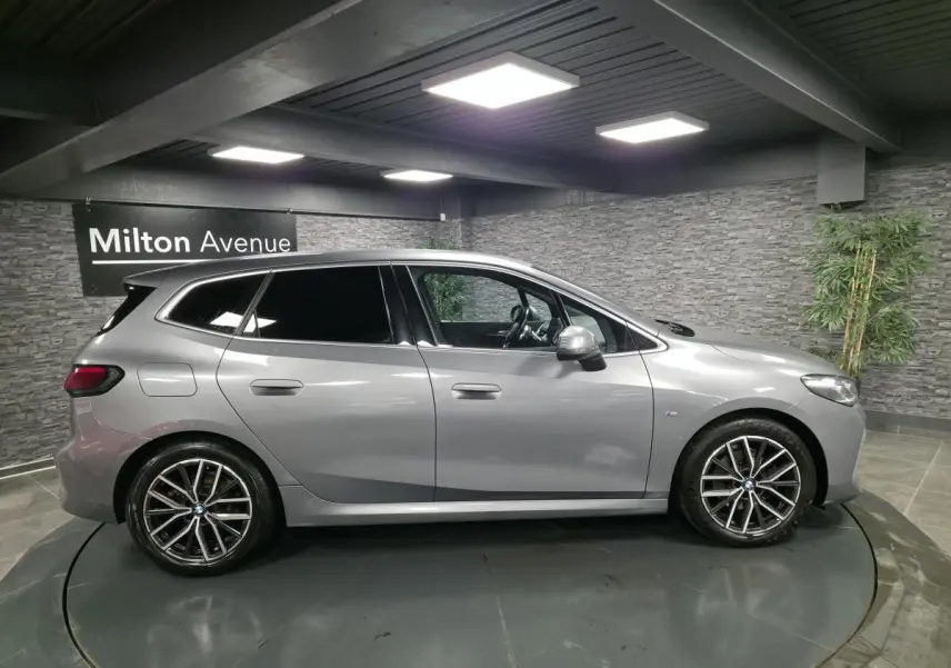BMW Série 2 218i Active Tourer gris métallisé vue de profil côté gauche en intérieur showroom.