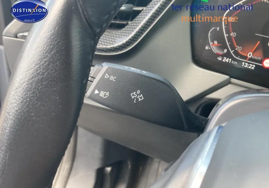 Gros plan sur la commande de clignotant et le volant cuir noir de la BMW Série 1 gris foncé, tableau de bord partiellement visible.
