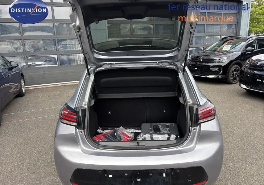 Vue arrière ouverte sur le coffre d'une Peugeot 208 électrique 2026 gris Artense métal, avec accessoires visibles à l'intérieur.