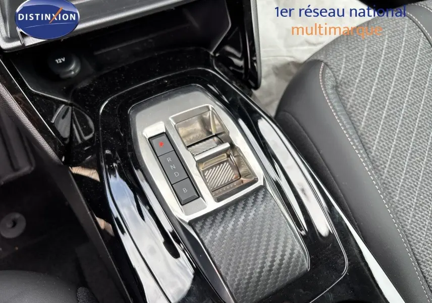 Gros plan sur la console centrale noire brillante avec sélecteur de vitesses électrique et siège tissu gris de la Peugeot 208 électrique.