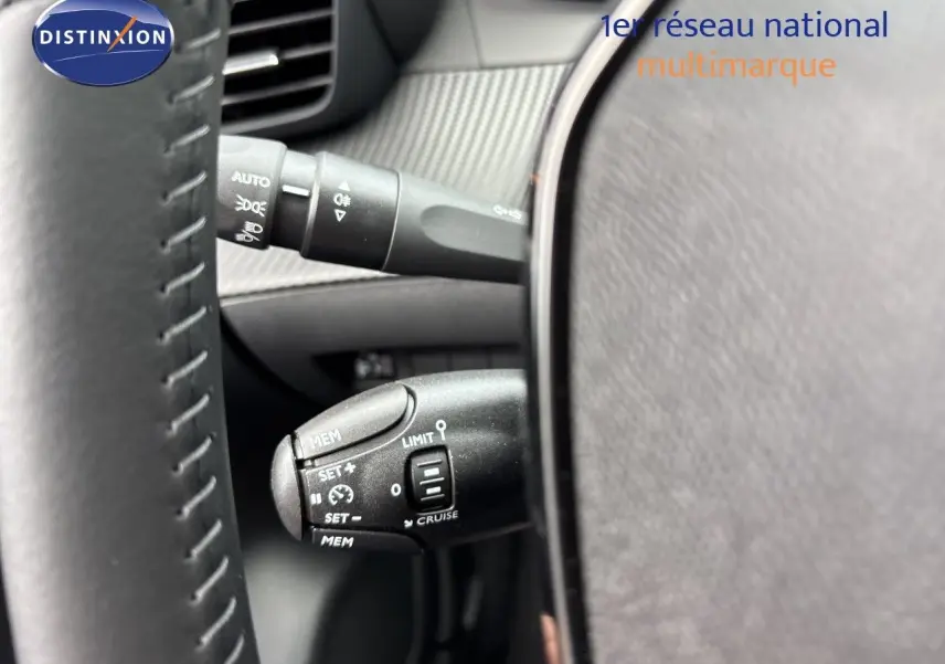 Gros plan sur la commande de régulateur de vitesse à gauche du volant d’une Peugeot 208 électrique gris Artense métal.