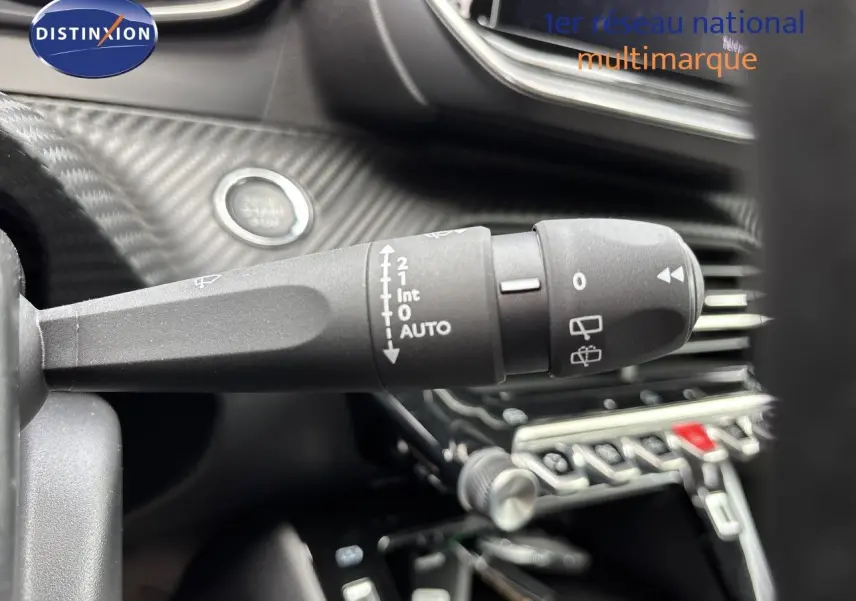 Gros plan sur la commande d’essuie-glace à gauche du volant dans l’habitacle noir d’une Peugeot 208 électrique gris Artense.