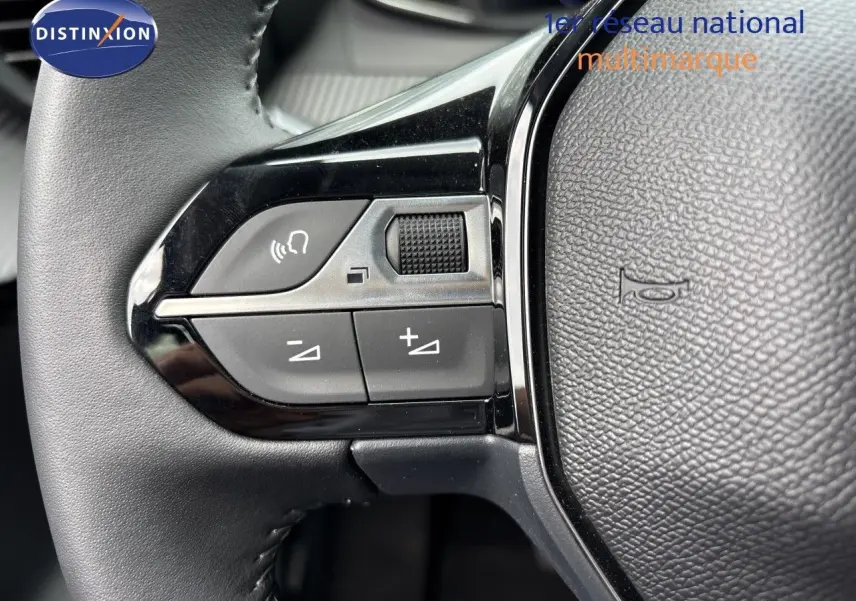 Gros plan sur les commandes gauche du volant cuir noir d’une Peugeot 208 électrique gris Artense, avec boutons de volume et téléphone.