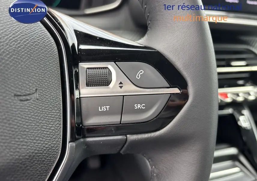 Gros plan sur les commandes gauche du volant cuir noir de la Peugeot 208 électrique gris Artense, avec boutons fonction audio et téléphone.