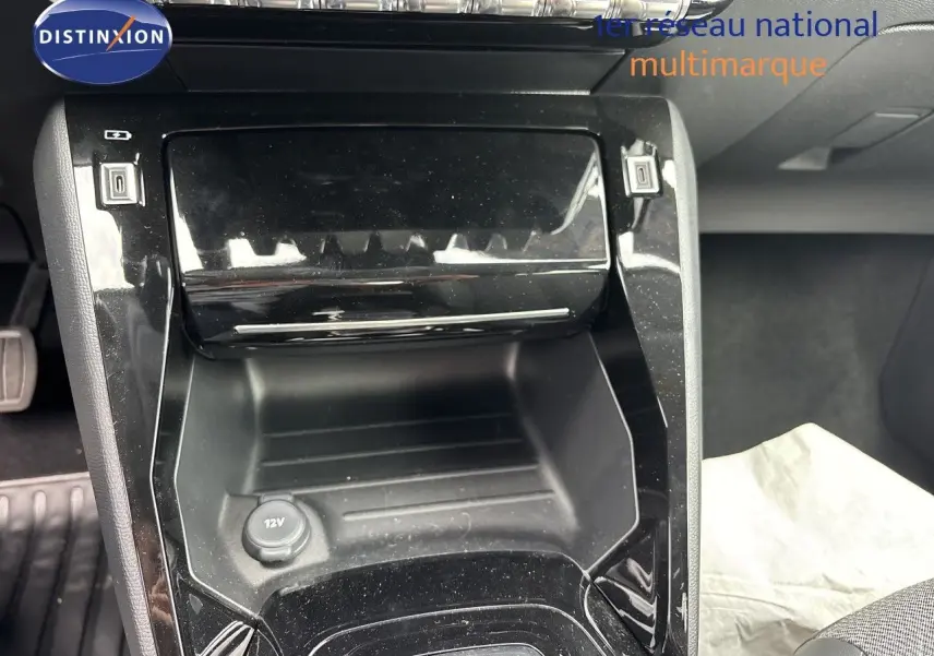 Gros plan sur la console centrale noire brillante de la Peugeot 208 électrique 2026, avec prise 12V visible.