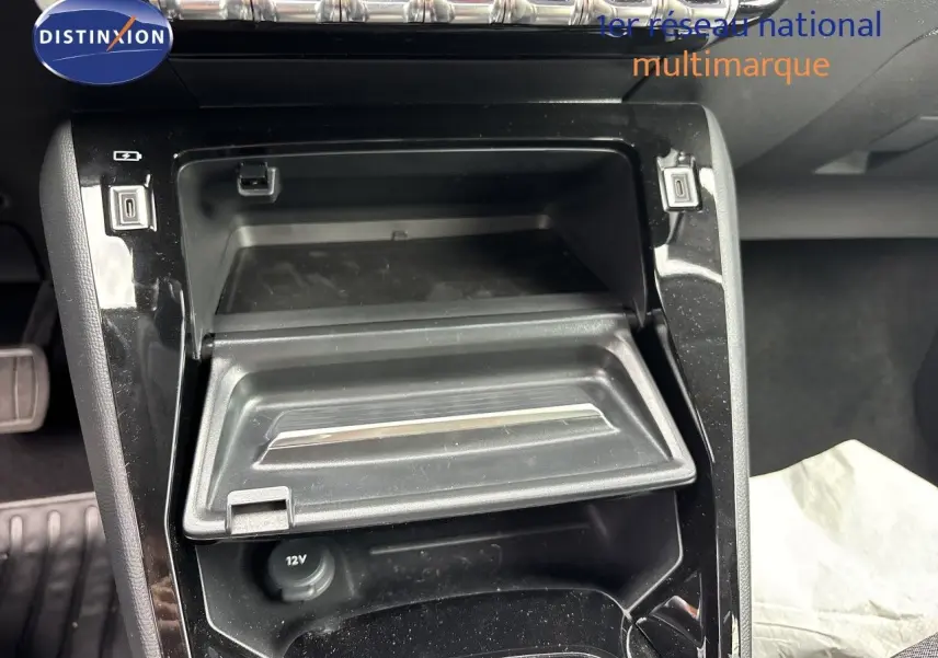Gros plan sur la console centrale de la Peugeot 208 électrique 2026, avec rangement ouvert et prises USB visibles.