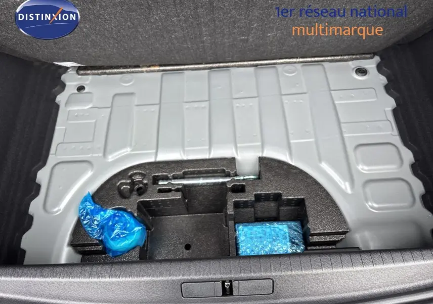Coffre ouvert d’une Peugeot 208 électrique gris Artense, vue plongeante sur le rangement sous plancher avec outils emballés.