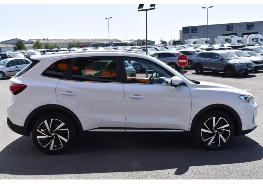 Vue de profil côté gauche d'un MG ZS blanc 2026 avec jantes alliage 18 pouces, garé en extérieur sur parking.