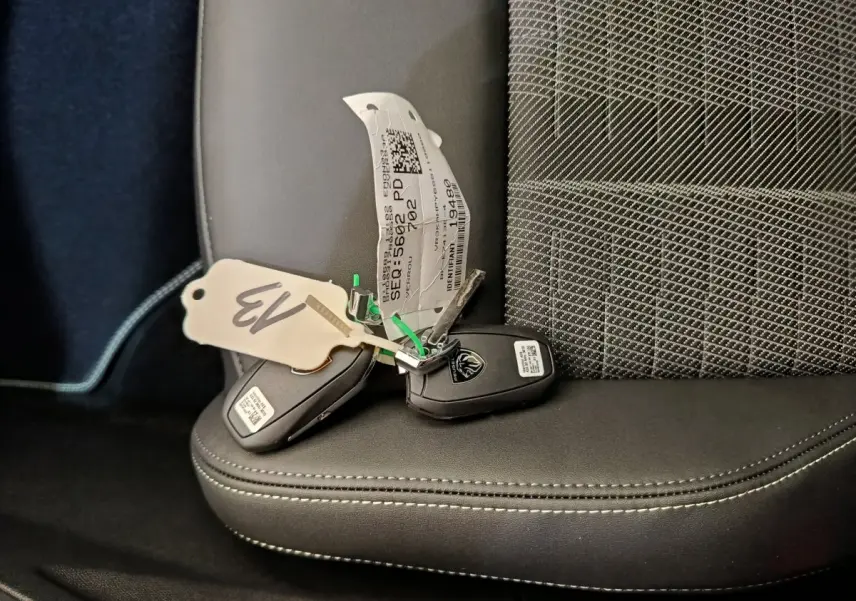 Clé de voiture Peugeot posée sur un siège avant en cuir noir avec surpiqûres blanches et tissu gris à motifs.