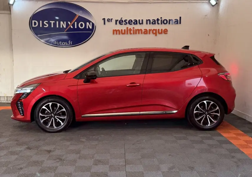Profil côté gauche d'une Renault Clio Techno TCe 90 rouge 2024, avec jantes alliage et feux arrière LED allumés.
