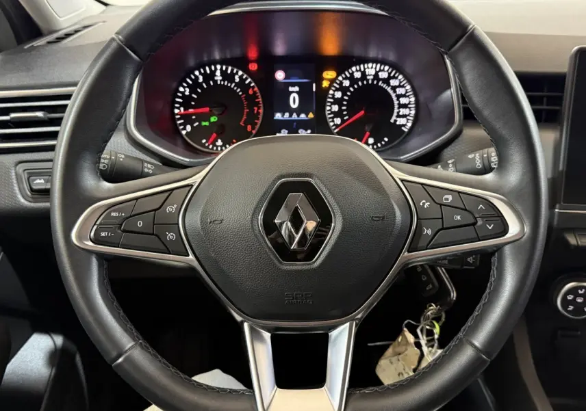 Vue rapprochée du volant cuir noir multifonctions d'une Renault Clio blanche avec tableau de bord et compteurs éclairés.